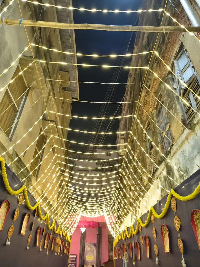A canopy of lights above our lane, late on Shashthi night