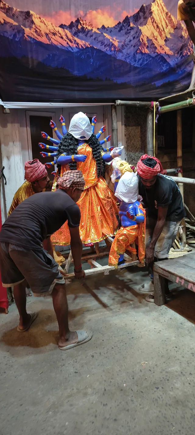 A goddess, her face still covered, is carried into the pandal